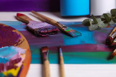 Photo of Colorful paints, wooden artist's palette and different brushes on white table, closeup