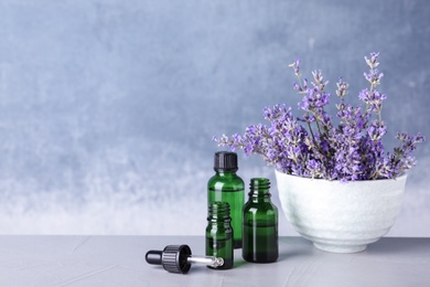 Photo of Bottles of essential oil and bowl with lavender flowers on stone table against blue background. Space for text