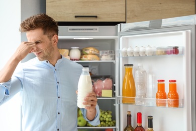 Photo of Man taking bottle with old milk out of refrigerator in kitchen