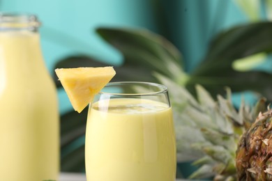 Photo of Tasty pineapple smoothie in glass and fruit against blurred background, closeup