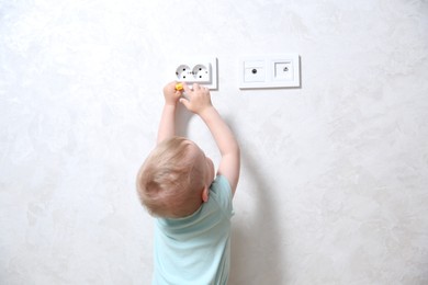 Photo of Little child playing with electrical socket indoors, back view. Dangerous situation