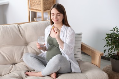 Beautiful pregnant woman holding pill and glass of water at home