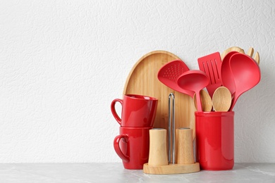 Set of kitchen utensils in stand on stone table near light wall. Space for text