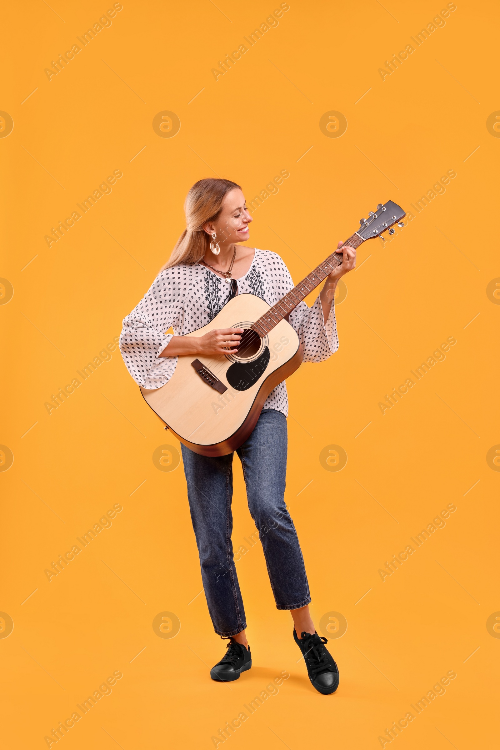 Photo of Happy hippie woman playing guitar on yellow background