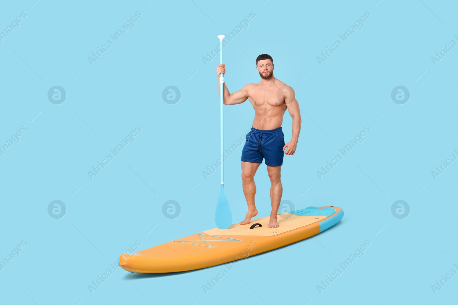 Photo of Handsome man with paddle on SUP board against light blue background