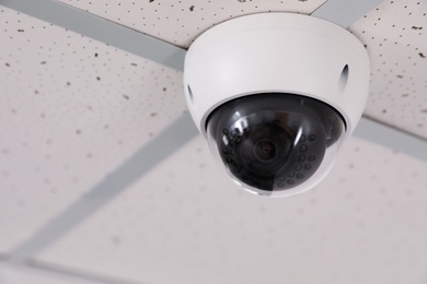 Photo of Modern security CCTV camera on ceiling in office, space for text. Protection system