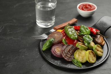 Delicious grilled vegetables with basil on black table