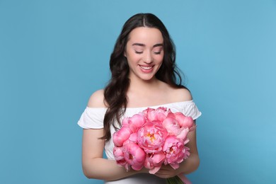 Photo of Beautiful young woman with bouquet of pink peonies on light blue background