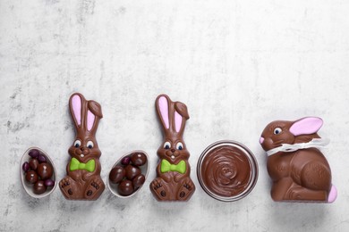 Photo of Flat lay composition with chocolate Easter bunnies, halved egg and candies on white textured table. Space for text