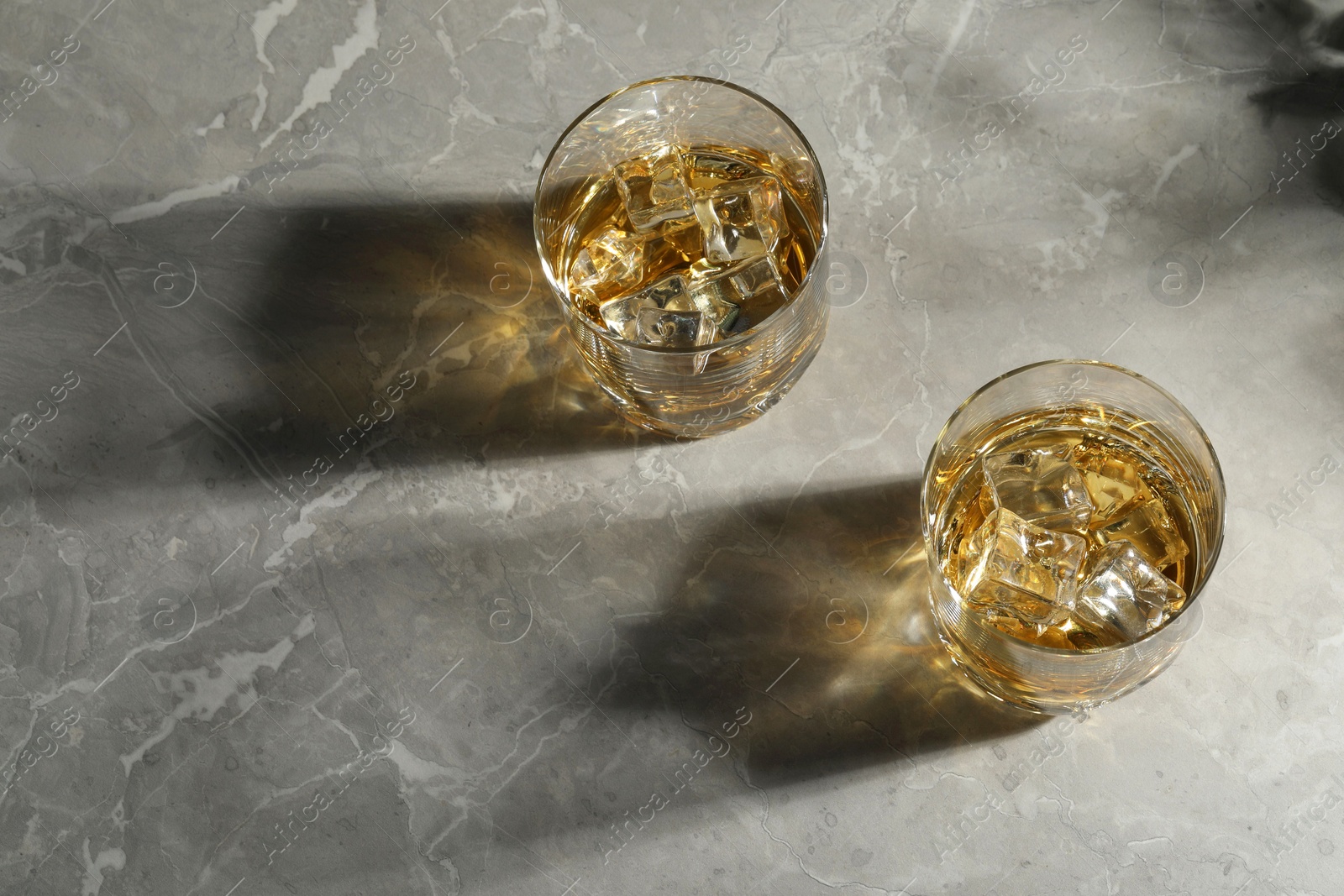 Photo of Whiskey with ice cubes in glasses on grey marble table, above view. Space for text