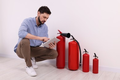 Photo of Man with tablet checking fire extinguishers indoors