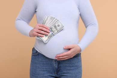 Photo of Surrogate mother. Pregnant woman with dollar banknotes on beige background, closeup