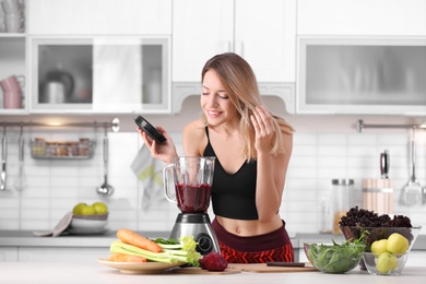 Photo of Young woman preparing tasty healthy smoothie at table in kitchen