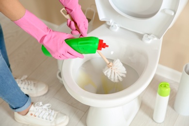 Photo of Woman cleaning toilet bowl in bathroom, closeup