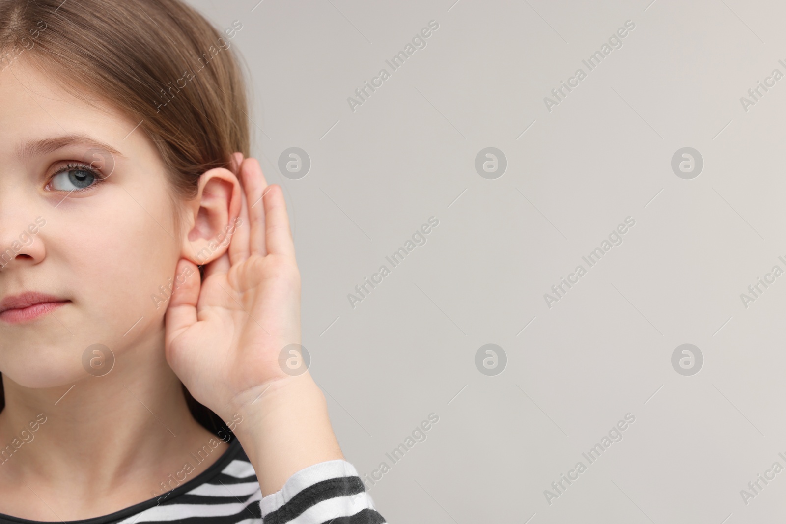 Photo of Little girl with hearing problem on grey background, closeup. Space for text