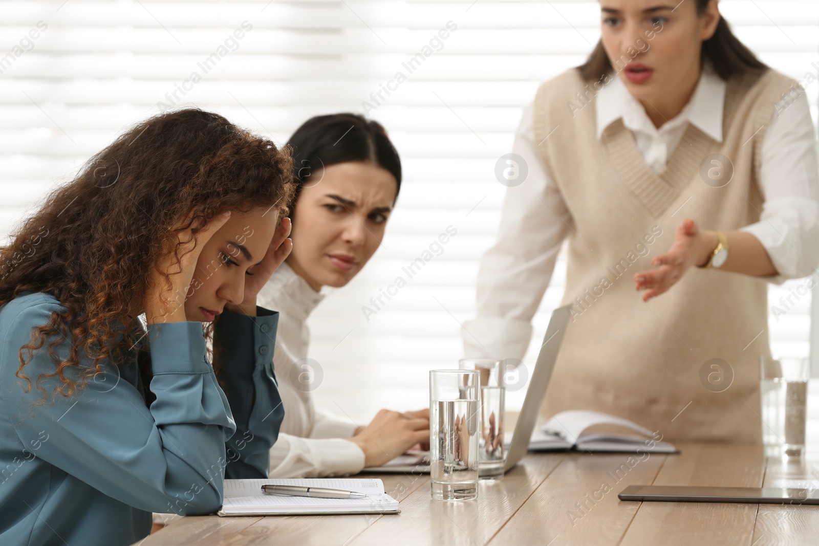 Photo of Woman screaming at African American coworker in office. Racism concept