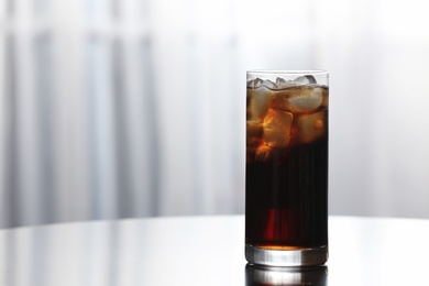 Photo of Glass of cola with ice on table against blurred background. Space for text