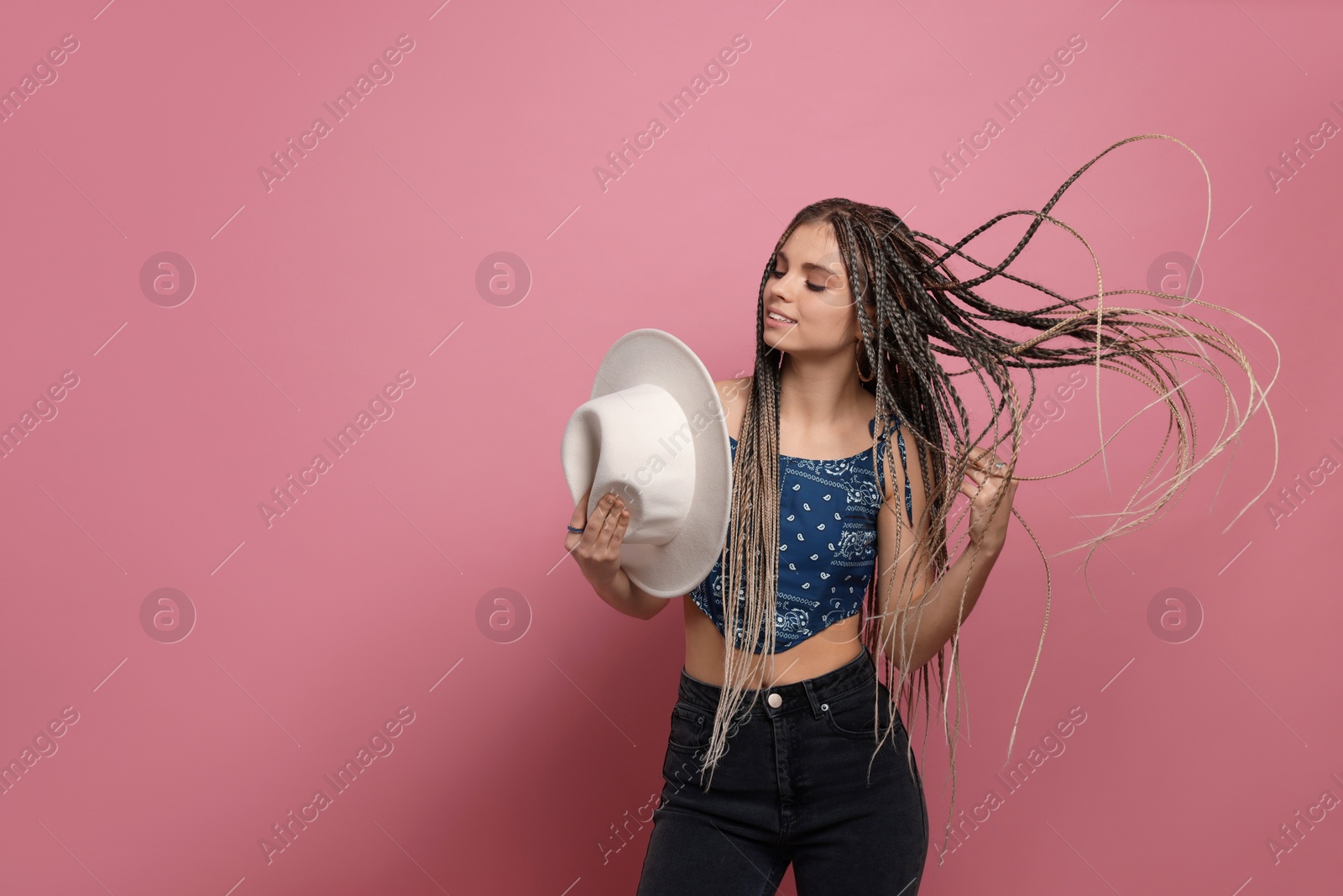 Photo of Beautiful woman with long african braids and hat on pink background, space for text