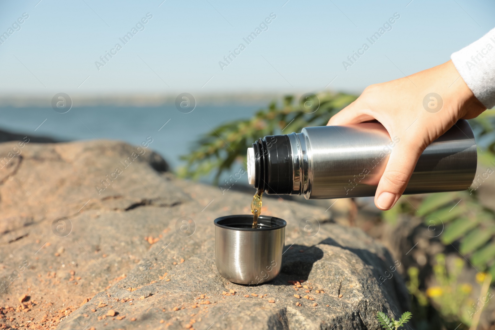 Photo of Woman pouring hot drink from thermos into cap outdoors, closeup