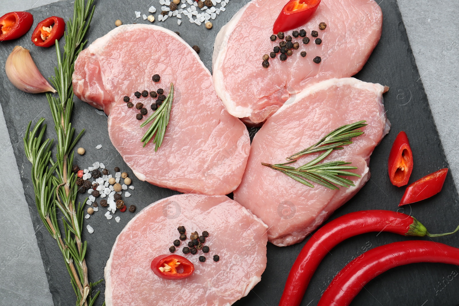 Photo of Pieces of raw pork meat, chili peppers and spices on grey table, top view