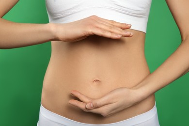 Photo of Woman holding hands near belly against green background, closeup
