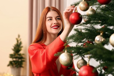 Beautiful young woman decorating Christmas tree at home