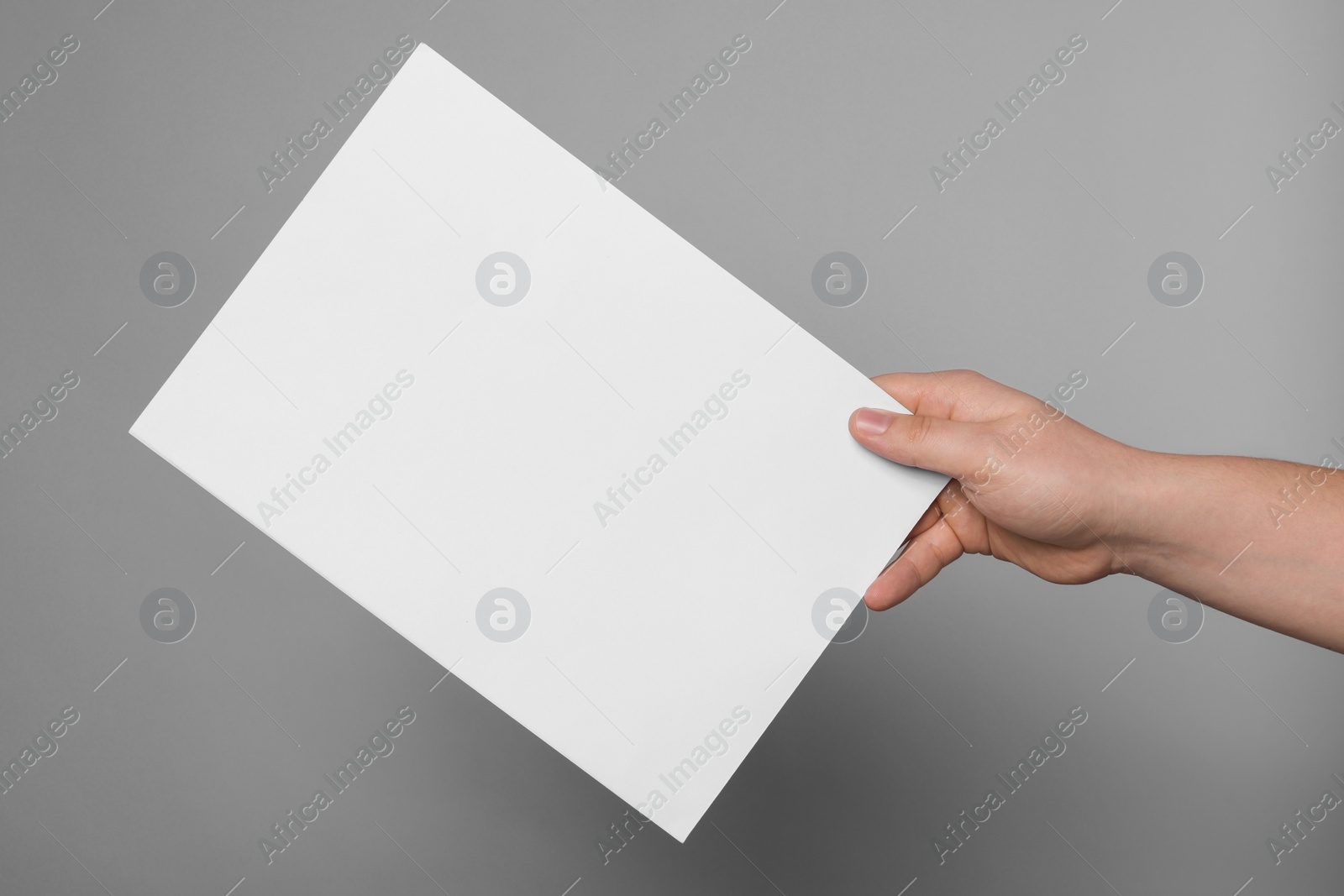 Photo of Woman holding sheet of paper on grey background, closeup. Mockup for design