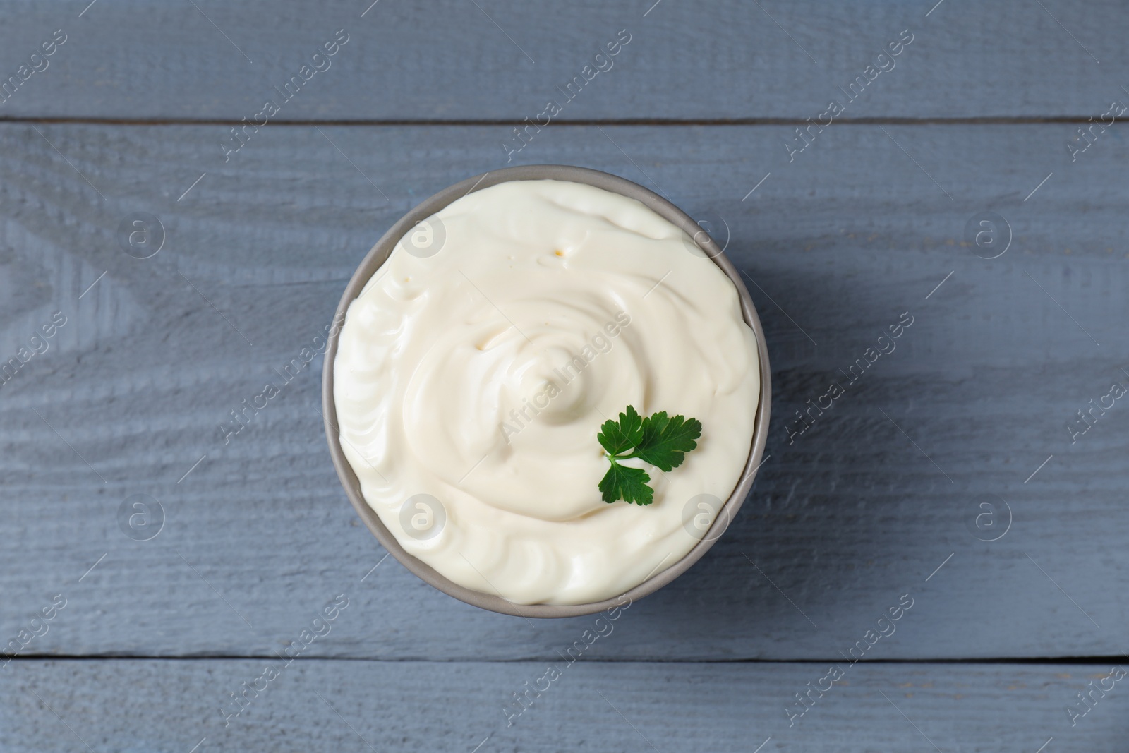 Photo of Tasty mayonnaise and parsley in bowl on gray wooden table, top view