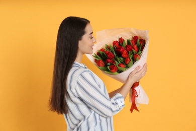 Photo of Happy woman with red tulip bouquet on yellow background. 8th of March celebration