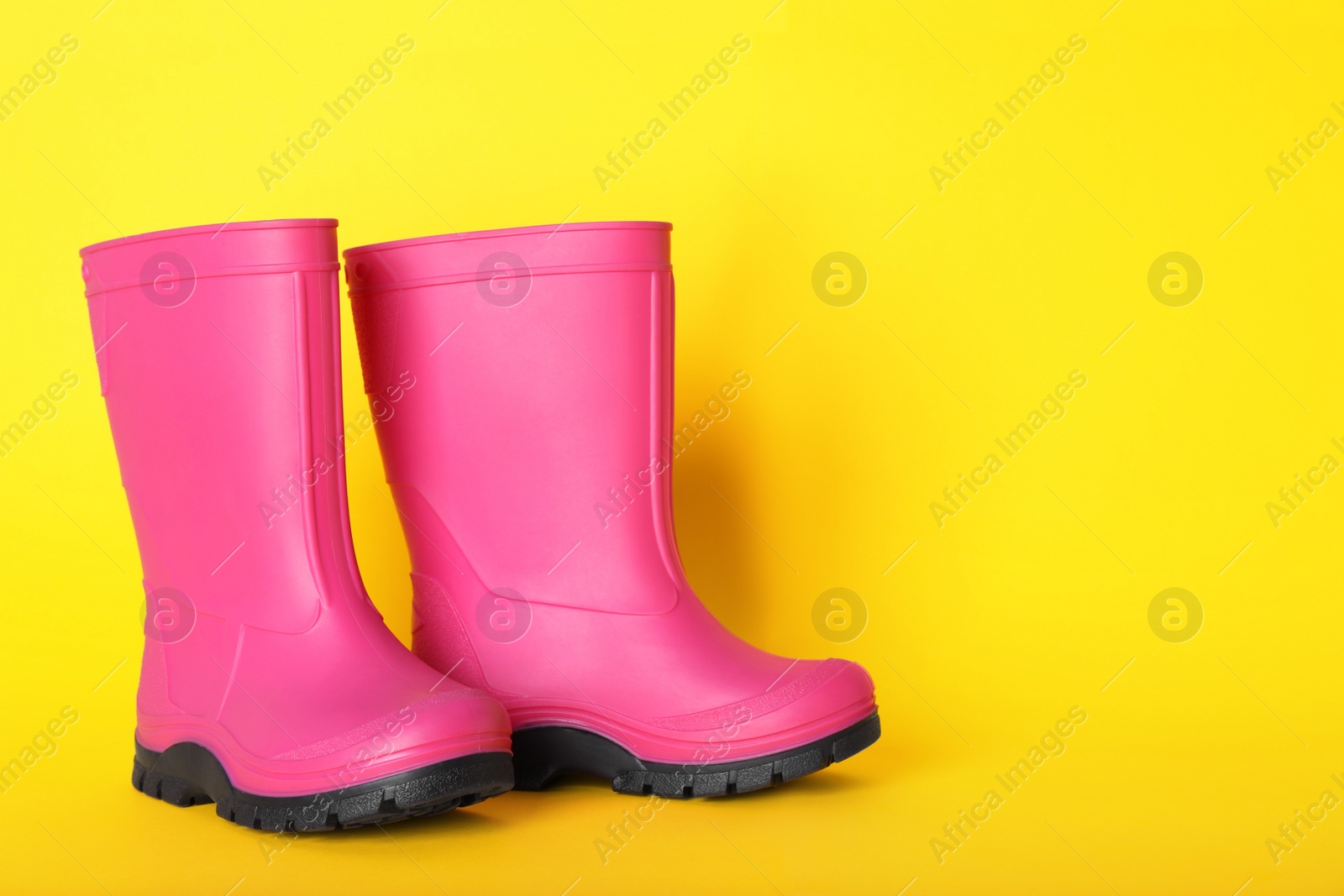 Photo of Pair of bright pink rubber boots on yellow background. Space for text