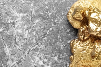 Photo of Pile of shiny gold nuggets on grey table, top view. Space for text