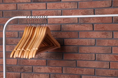 Photo of Wooden clothes hangers on rack near red brick wall. Space for text