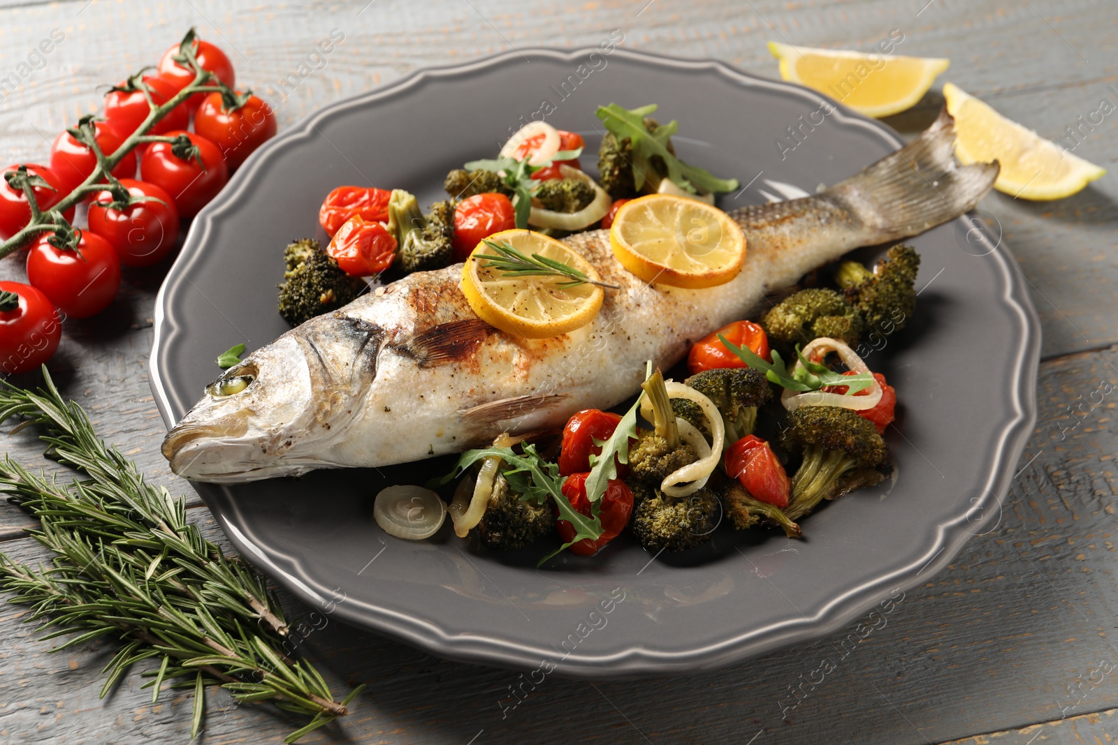 Photo of Baked fish with vegetables, rosemary and lemon on grey wooden table, closeup