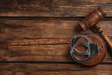 Photo of Flat lay composition with handcuffs and gavel on wooden table, space for text. Criminal law