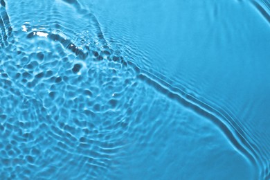 Rippled surface of clear water on light blue background, closeup