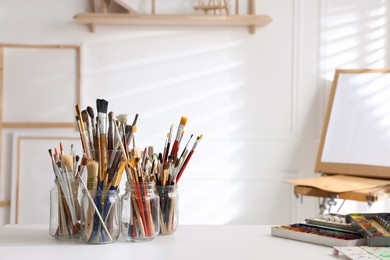Photo of Different brushes, paints and palette on white table indoors, space for text. Artist's workplace