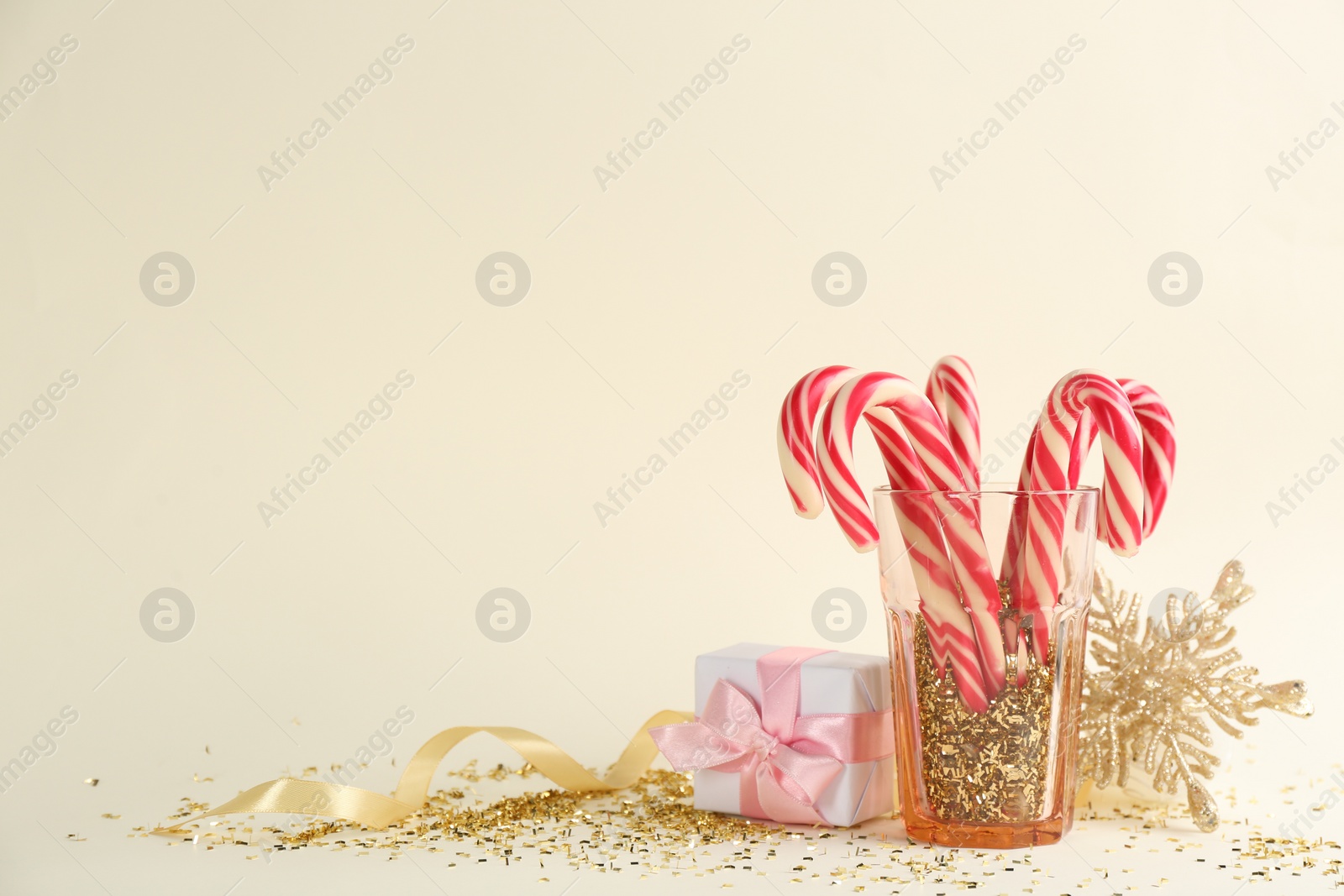 Photo of Christmas candy canes, gift box and confetti on beige background, space for text