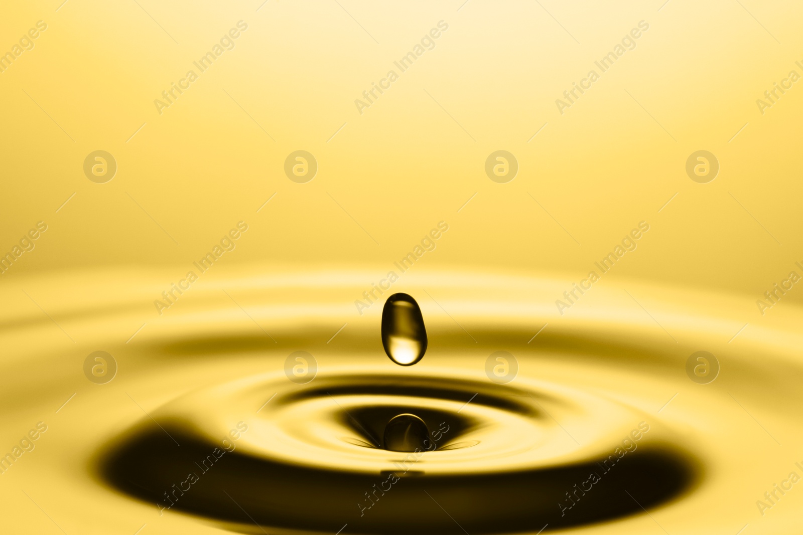 Image of Splash of golden oily liquid with drop on yellow background, closeup