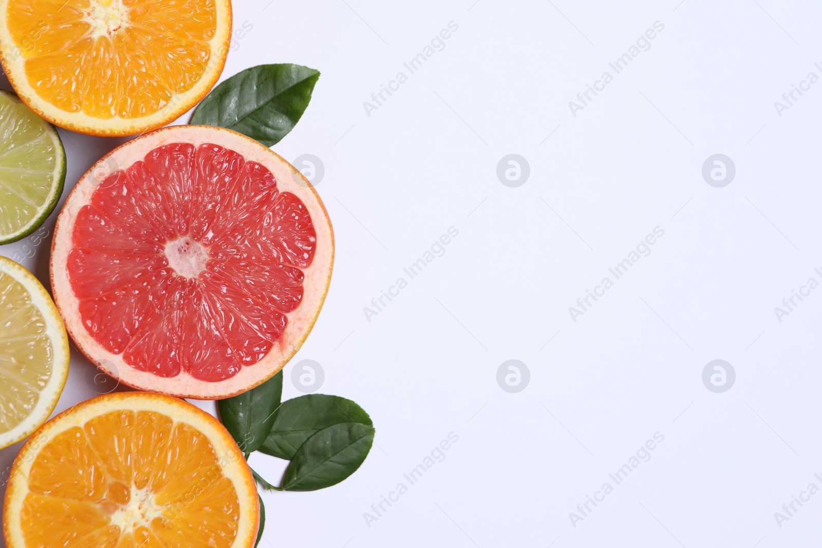 Photo of Different cut citrus fruits and leaves on white table, flat lay. Space for text