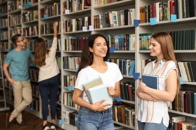 Photo of Young people standing near bookshelves in library