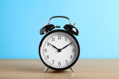 Photo of Black alarm clock on wooden table against light blue background