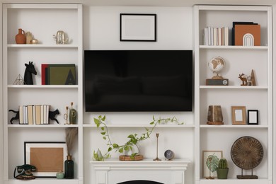 Stylish shelves with different decor elements and TV set in living room. Interior design