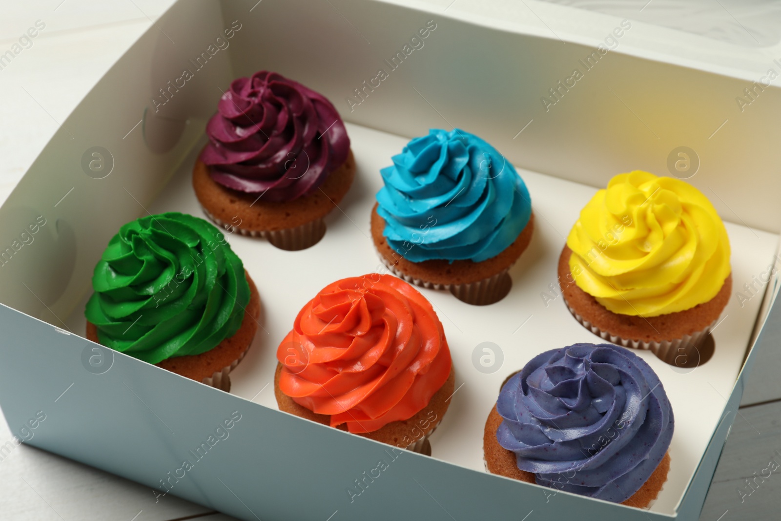 Photo of Box with different cupcakes on white wooden table, closeup