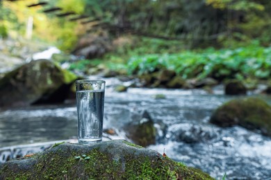 Glass of fresh water on stone with moss near stream. Space for text