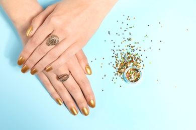 Photo of Woman showing manicured hands with golden nail polish and glitter on color background, top view