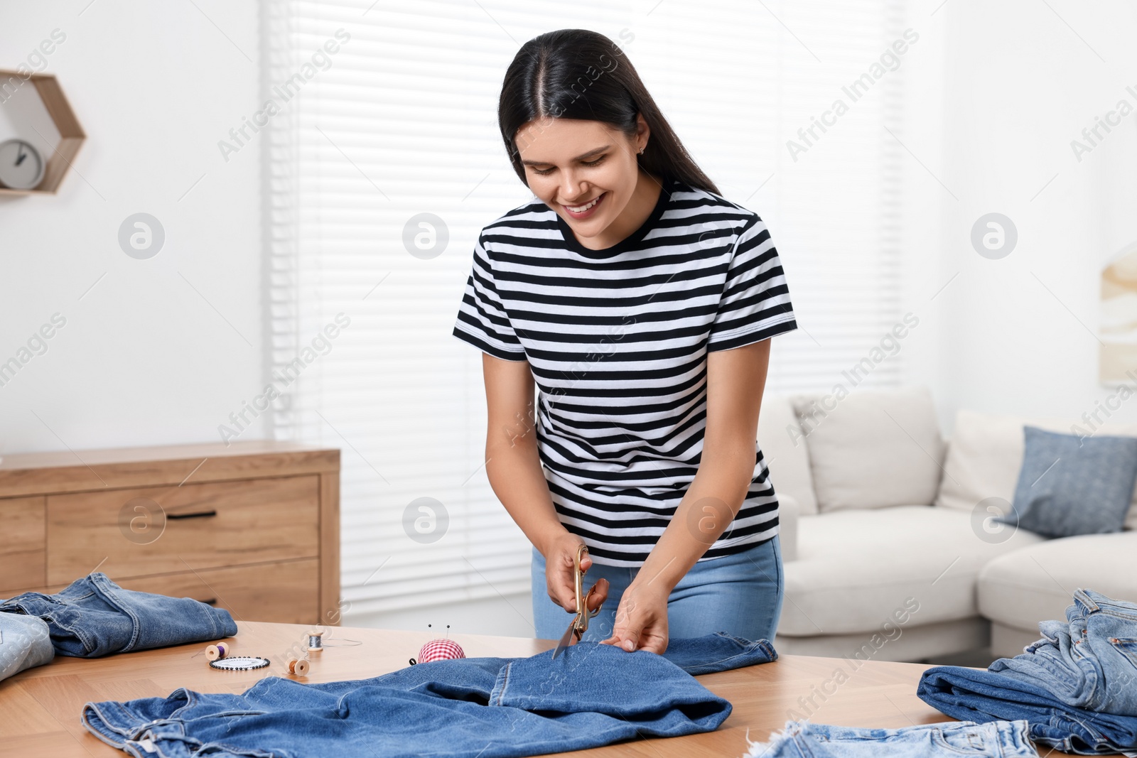 Photo of Young woman cutting jeans with scissors at wooden table indoors