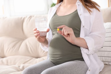 Photo of Pregnant woman holding pill and glass with water at home, closeup