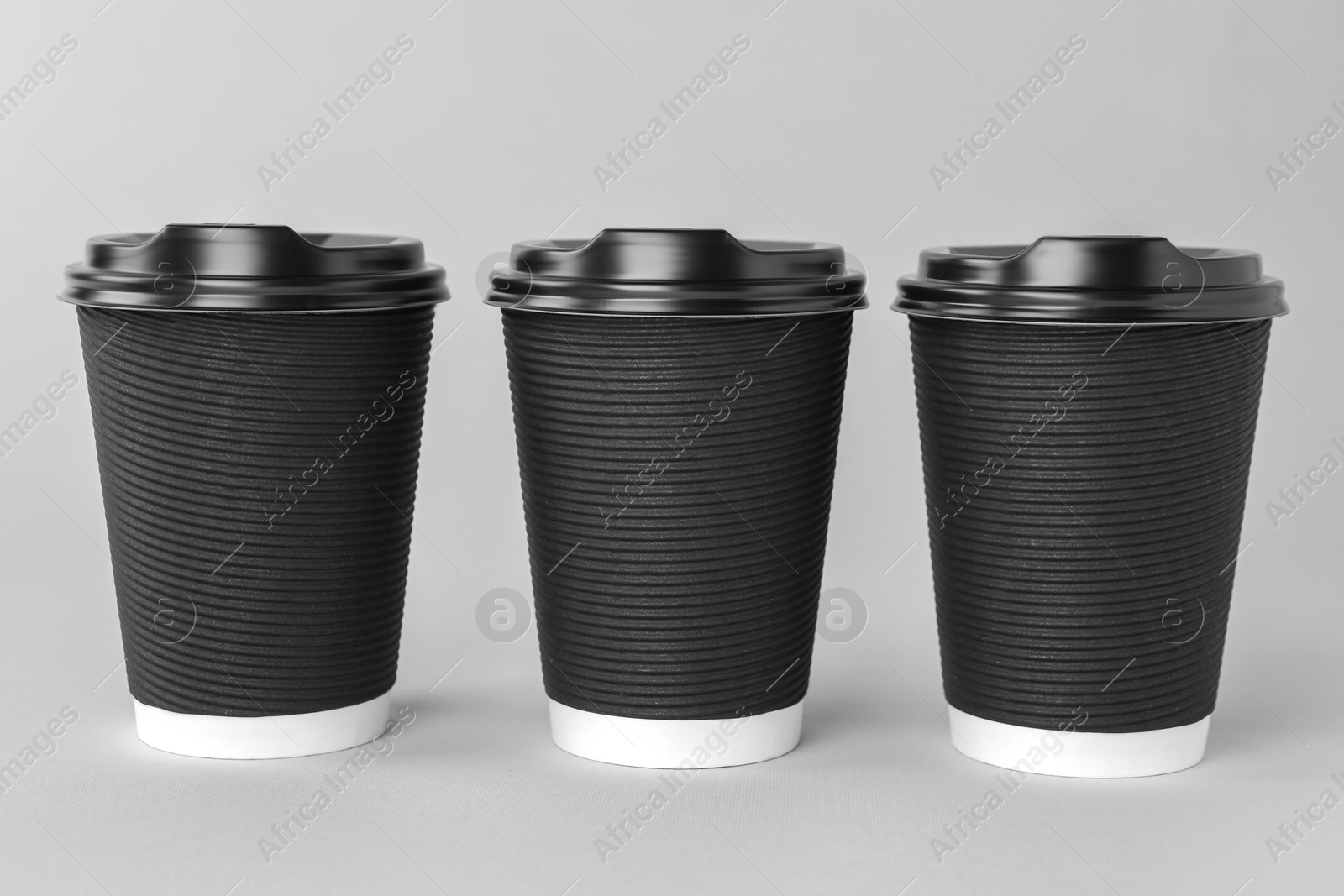 Photo of Paper cups with black lids on light grey background. Coffee to go