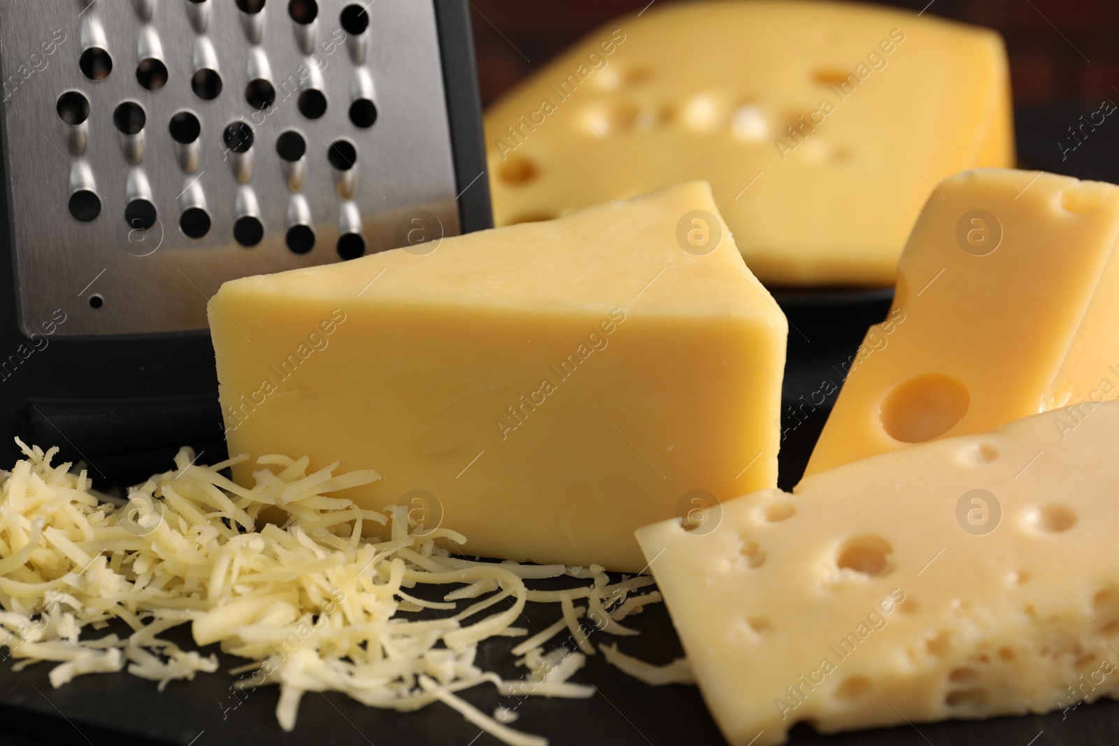 Photo of Grated, cut cheese and grater on black table, closeup