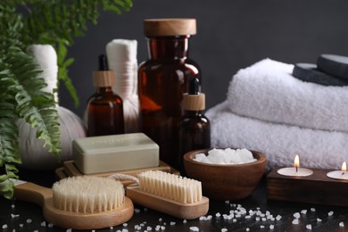 Photo of Spa composition. Brushes, soap bar, sea salt and burning candles on black table